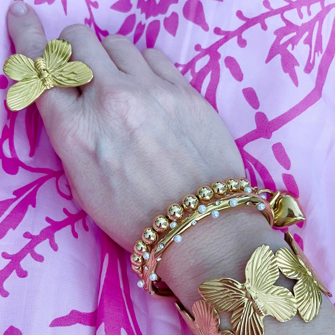 a woman's arm and hand wearing a gold butterfly cuff, gold bracelets, and a gold butterfly cocktail ring