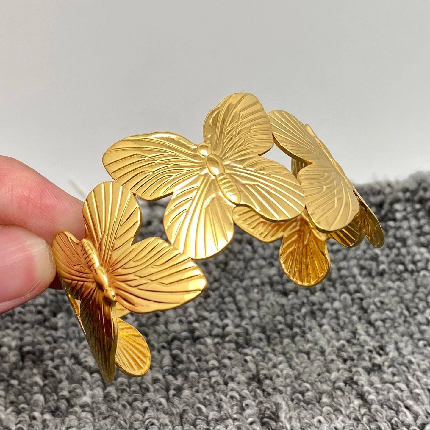 two fingers holding a gold butterfly cuff