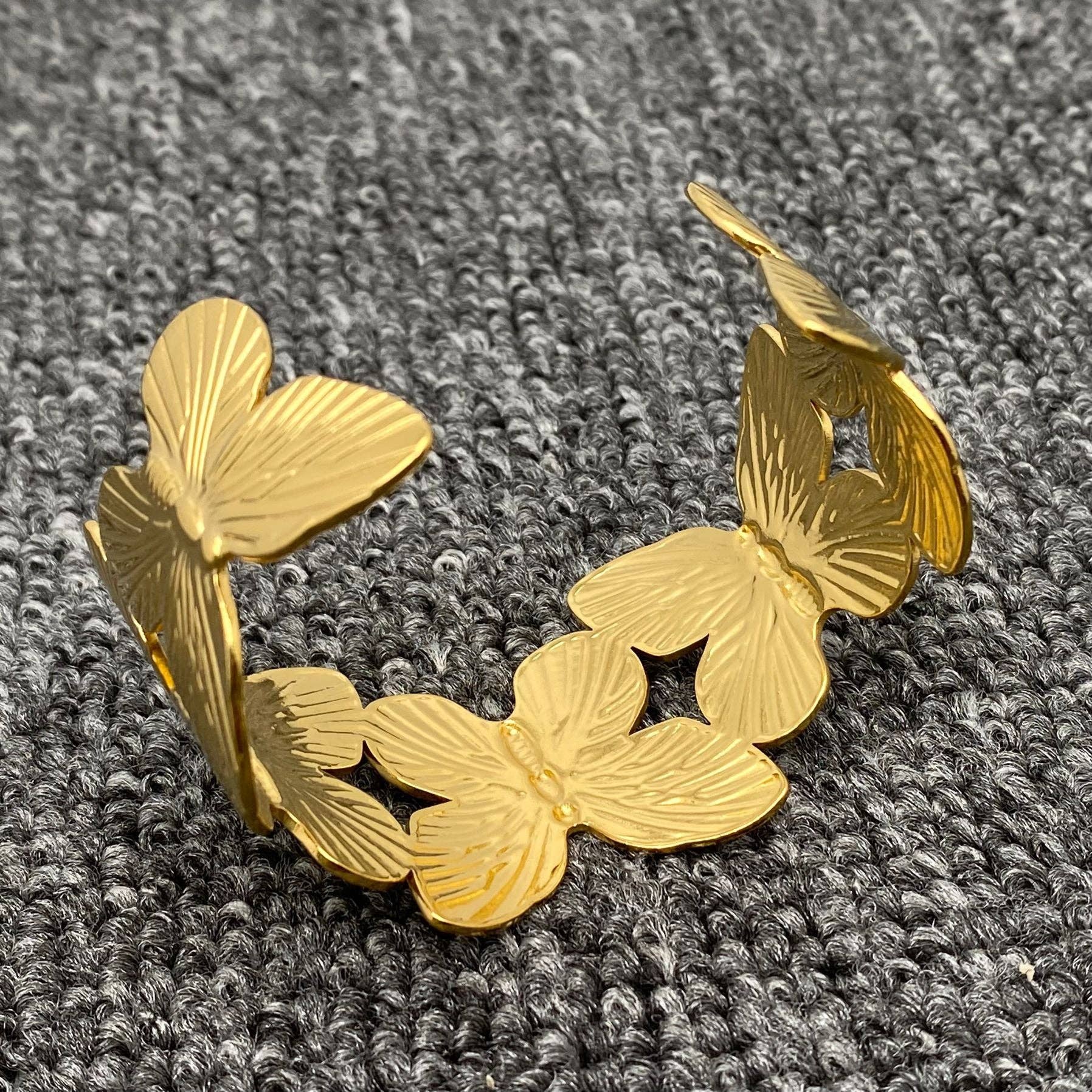 the underside view of a gold butterfly cuff bracelet on grey carpet