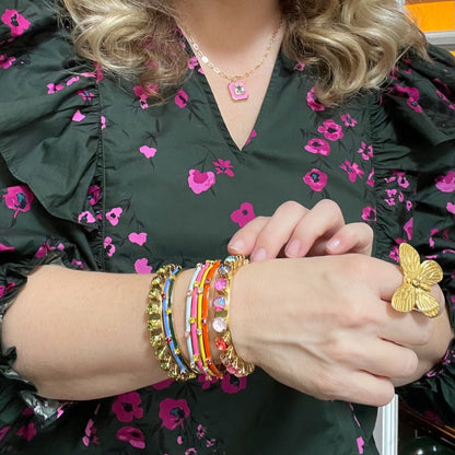 woman in green and pink floral blouse and gold butterfly ring with multiple crystal bracelets