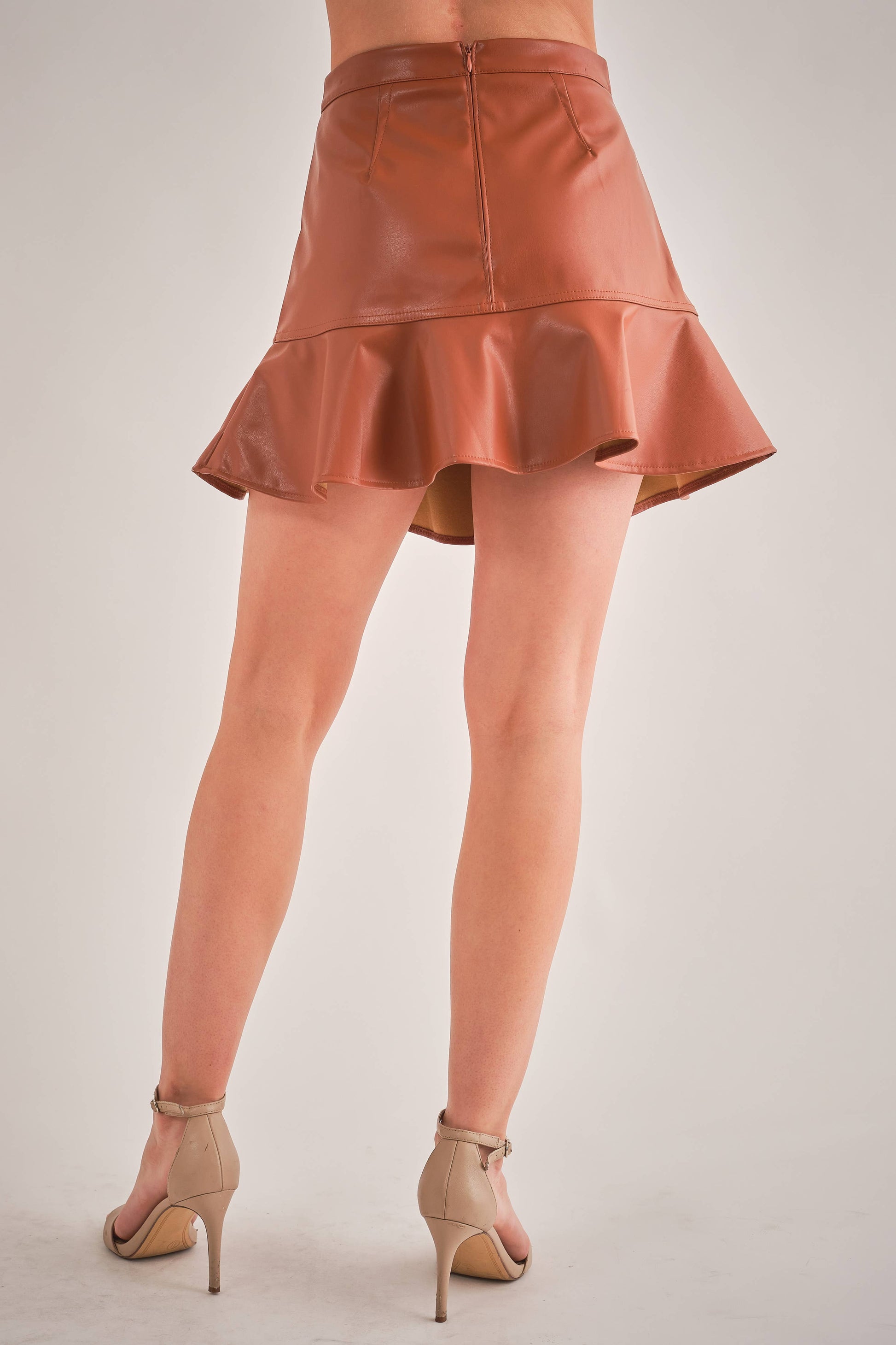 back view of woman wearing brown vegan leather mini skirt and tan heels